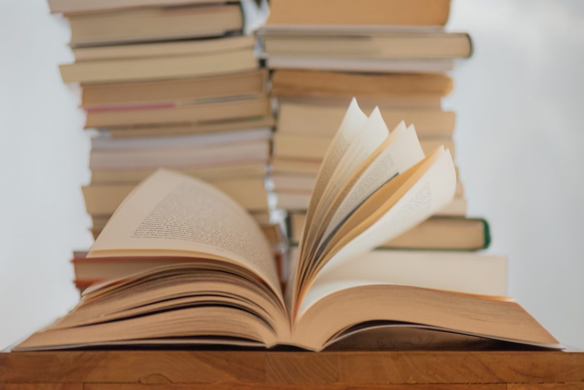 Many of the best author resources come in book-form, like the stack of books in this image. An open book sits in front of two tall stacks, with its pages spread open.