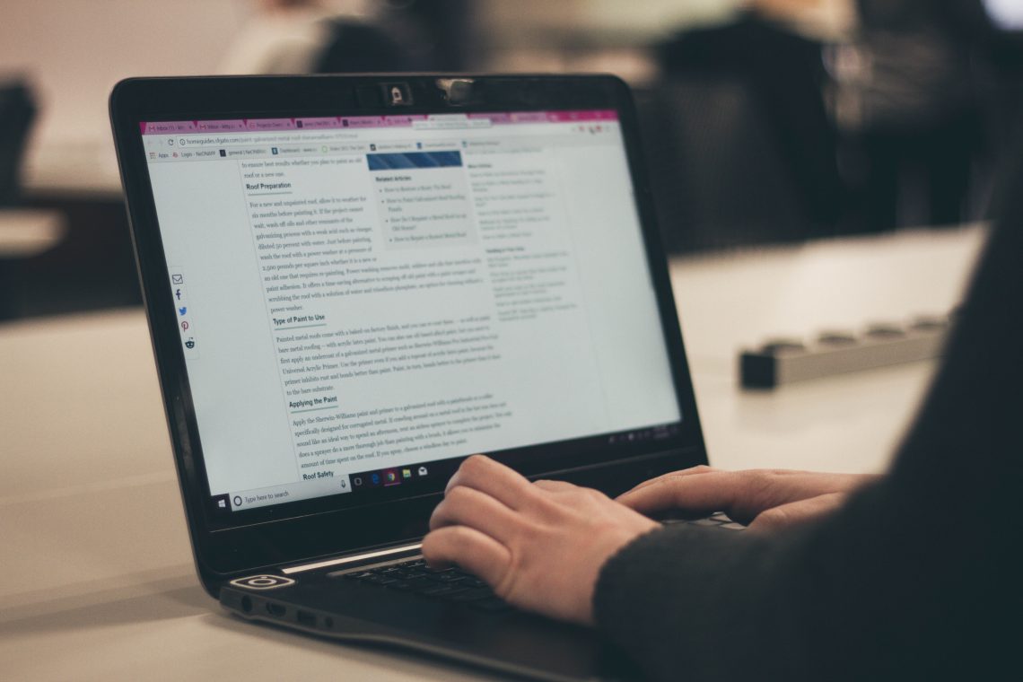 A blogger sits at her desk, looking at an article about blog monetization strategies on a black laptop.