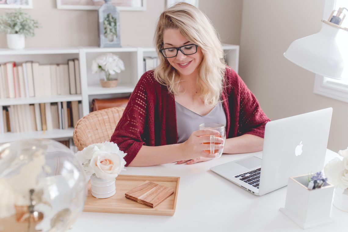 A full-time freelancer sits at her desk with her laptop in front of her, a cup of hot tea in hand.