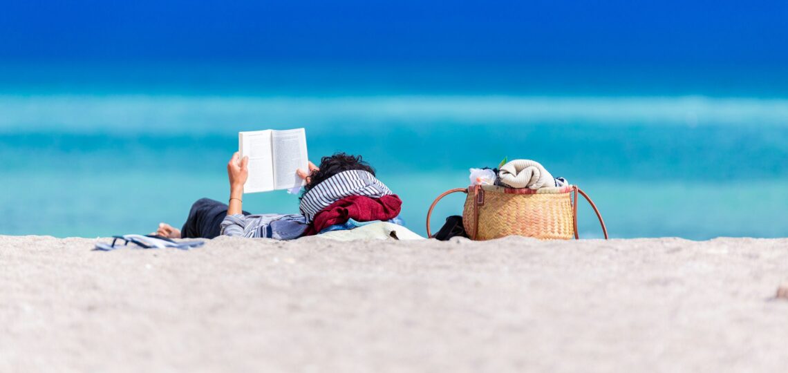 A person lying on the beach, reading a book.