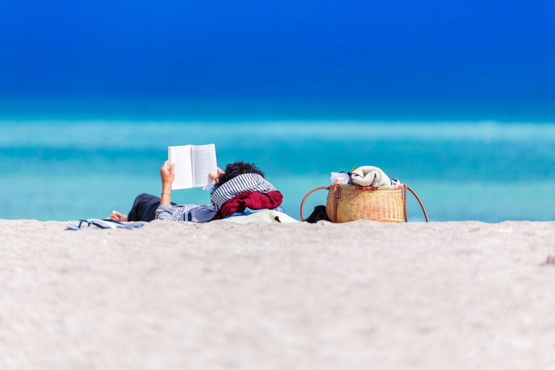A person lying on the beach, reading a book.