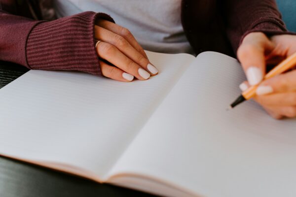 A woman's hands rest on a blank notebook page, one hand grasping a pen.