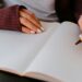 A woman's hands rest on a blank notebook page, one hand grasping a pen.