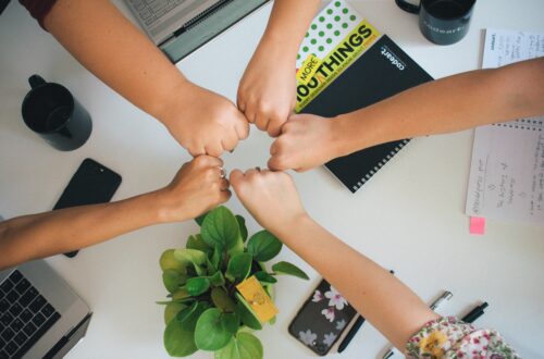 A group of people put their hands into a center circle, signifying teamwork.