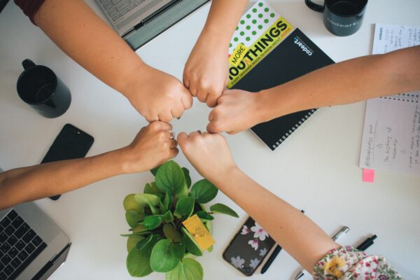 A group of people put their hands into a center circle, signifying teamwork.